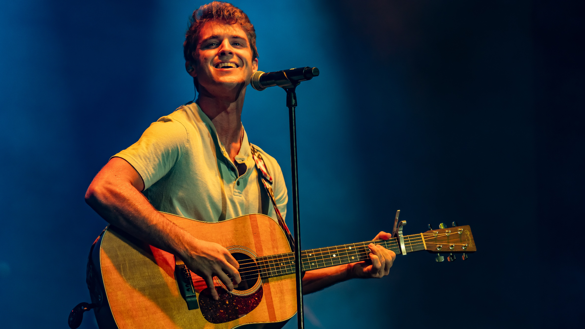 Michael Patrick Joyce smiling while playing acoustic guitar in amber light
