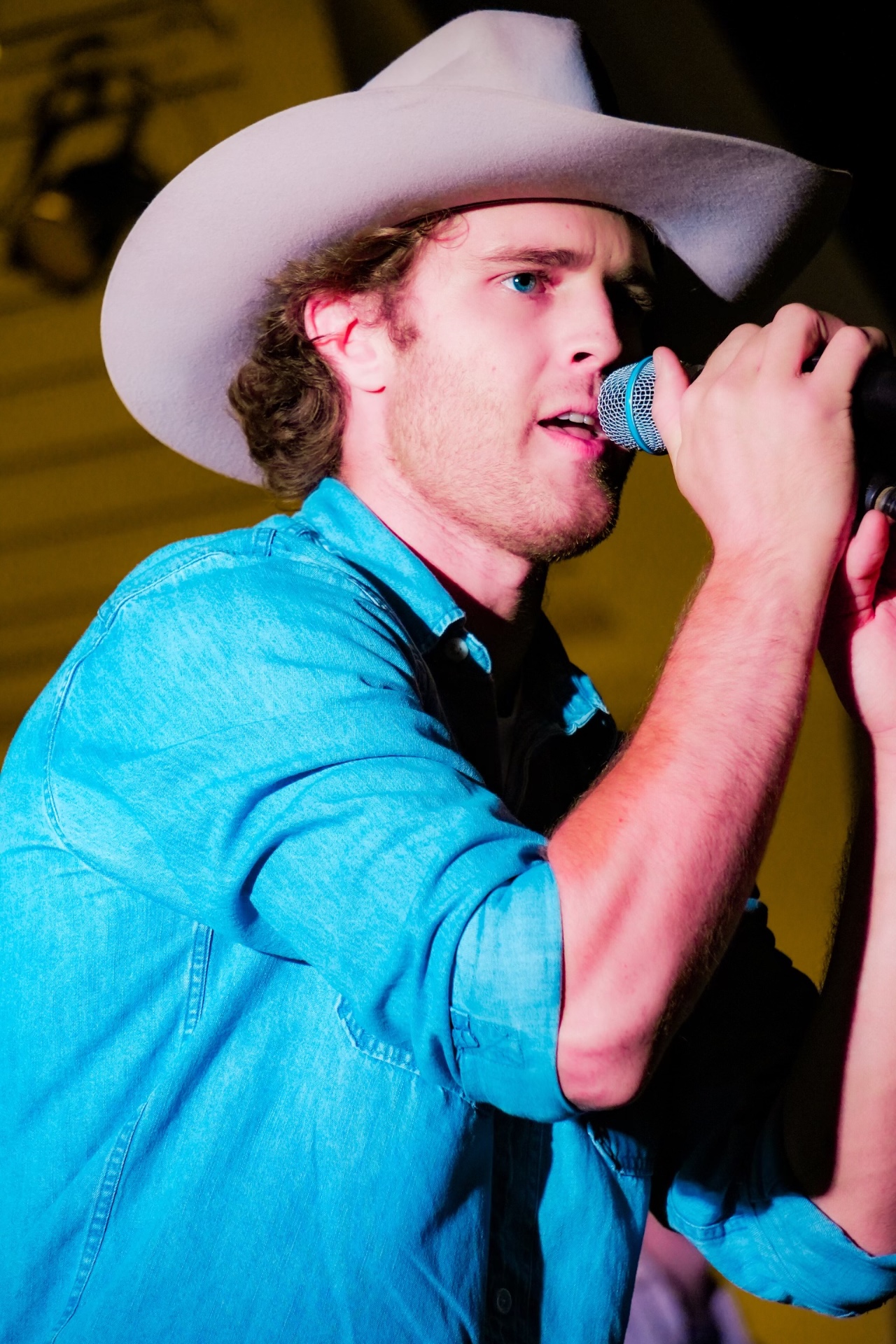 Michael Patrick Joyce singing into a handheld microphone wearing a denim shirt