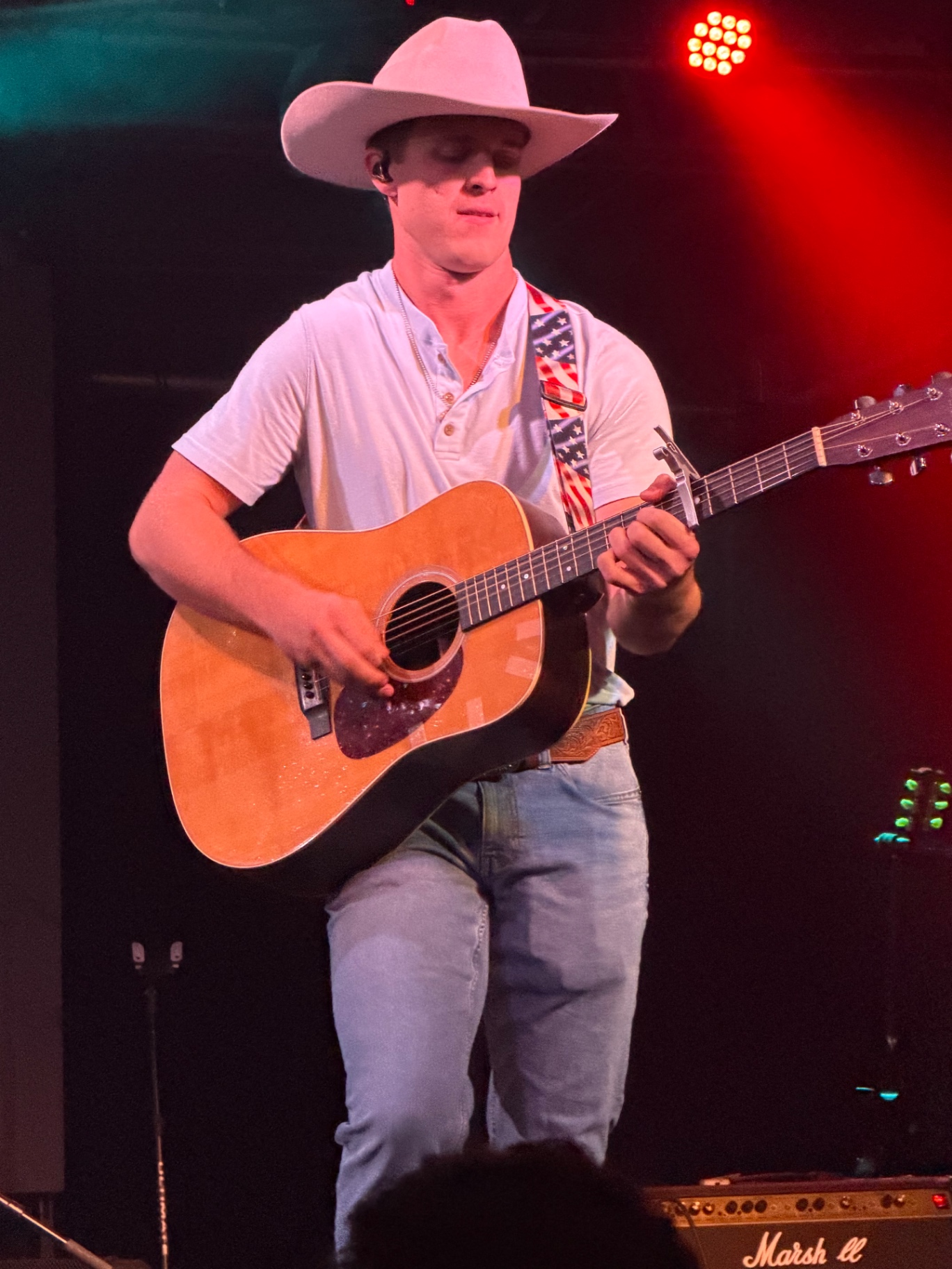 Michael Patrick Joyce playing guitar under red stage light in a white cowboy hat